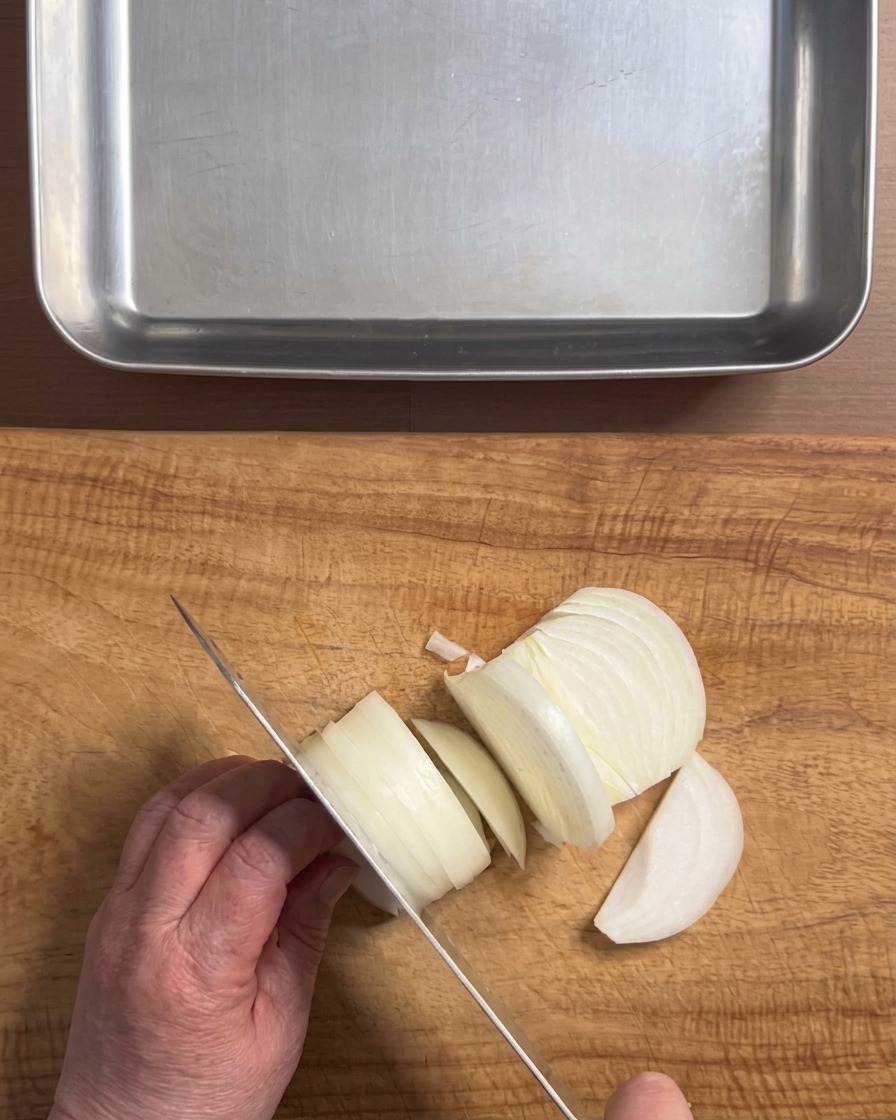 Mani che usano un coltello per tagliare una cipolla bianca a strisce spesse su un tagliere di legno.
