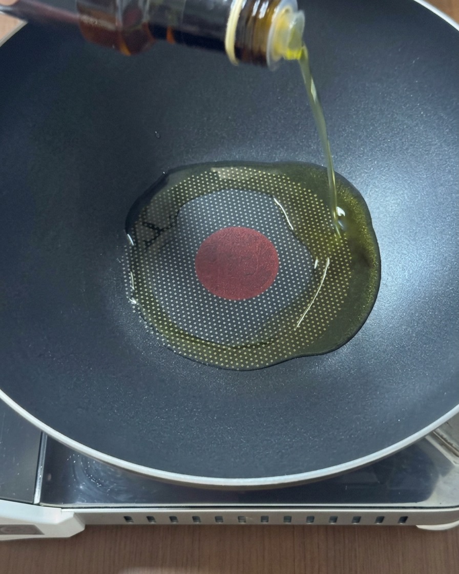 Olio dorato che viene versato da una bottiglia di vetro al centro di un wok nero scaldato.