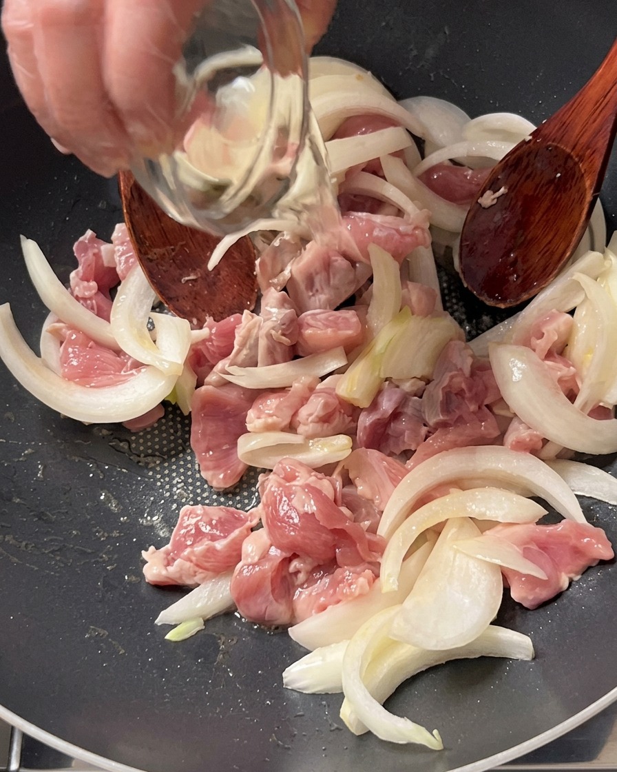 Vino da cucina versato da una ciotolina di vetro sopra la carne di maiale e le cipolle in padella.