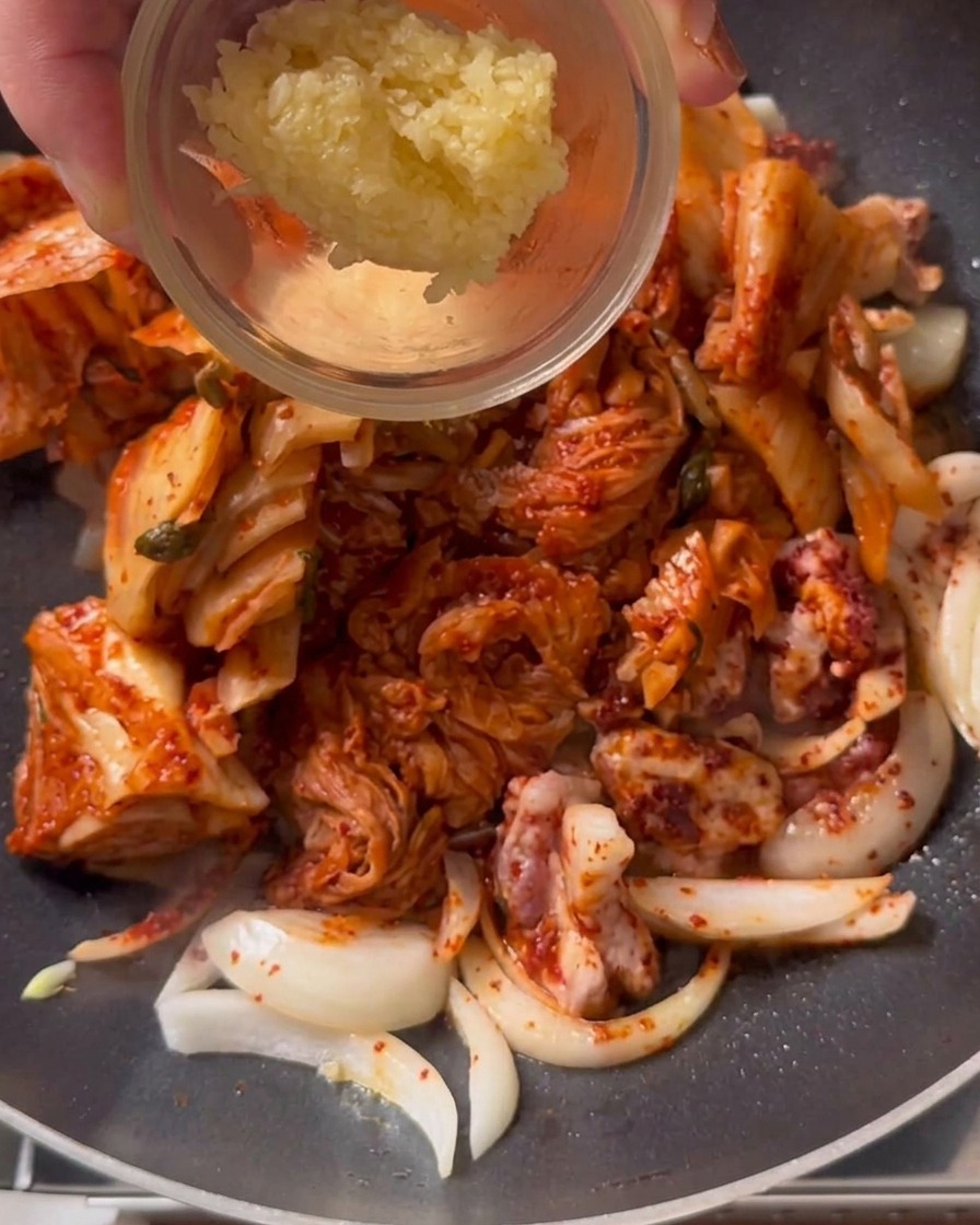 Un cucchiaio di aglio tritato aggiunto a una padella di kimchi e maiale saltati.