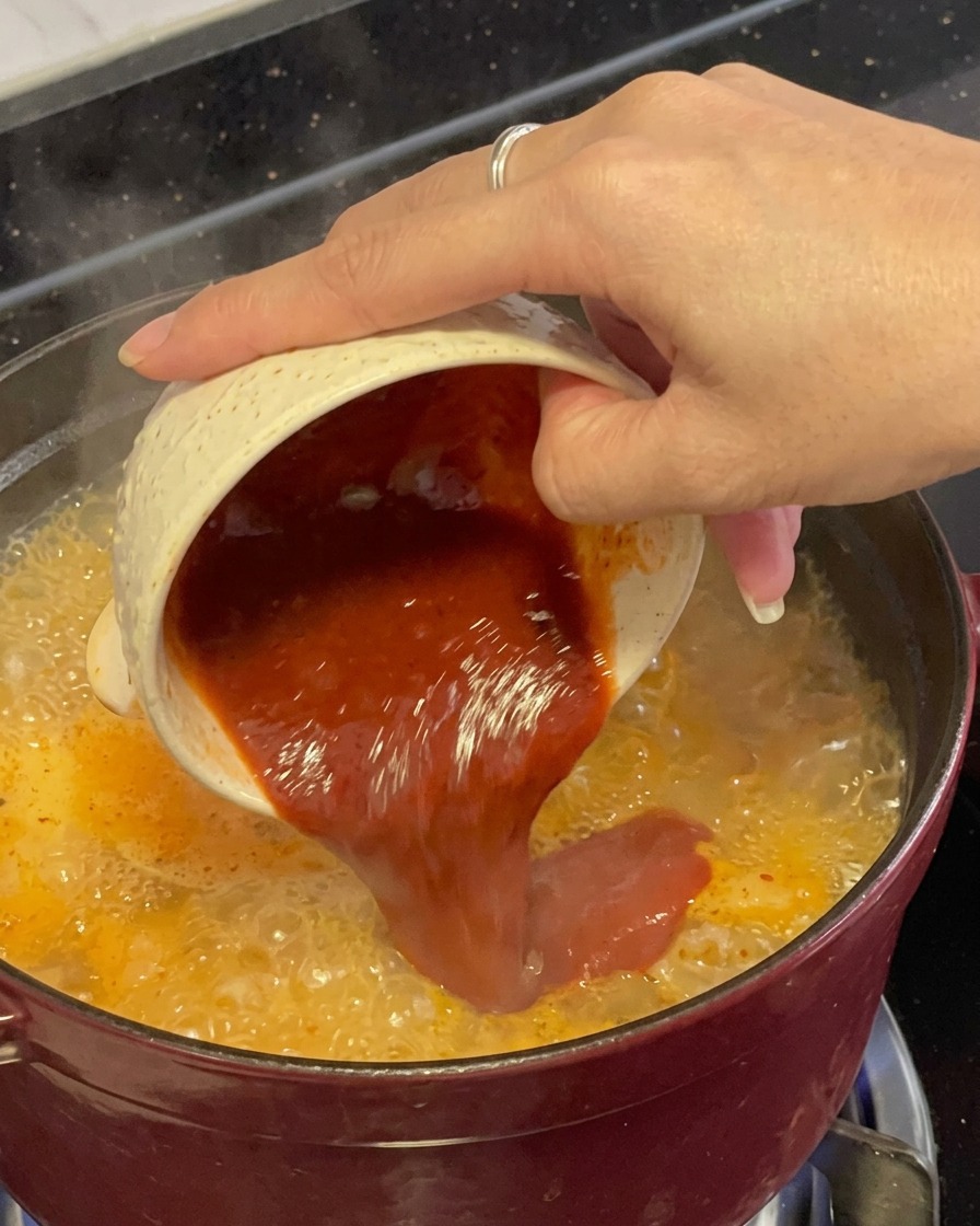 Una miscela di condimento densa e rosso scuro versata da una ciotolina direttamente nello stufato di pesce rosso che bolle.