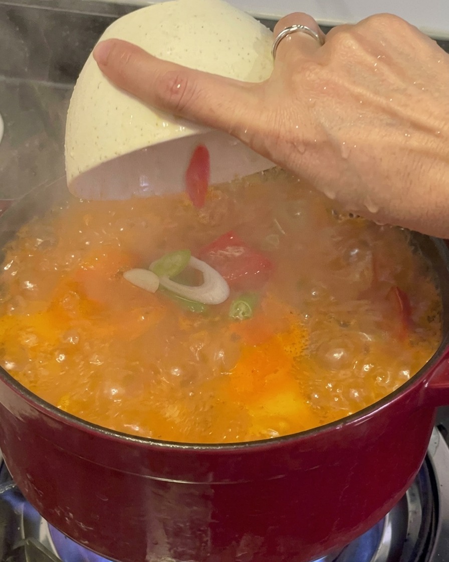 Cipollotti freschi affettati e peperoncini rossi distribuiti da una ciocola bianca sopra uno stufato di kimchi fumante e bollente.