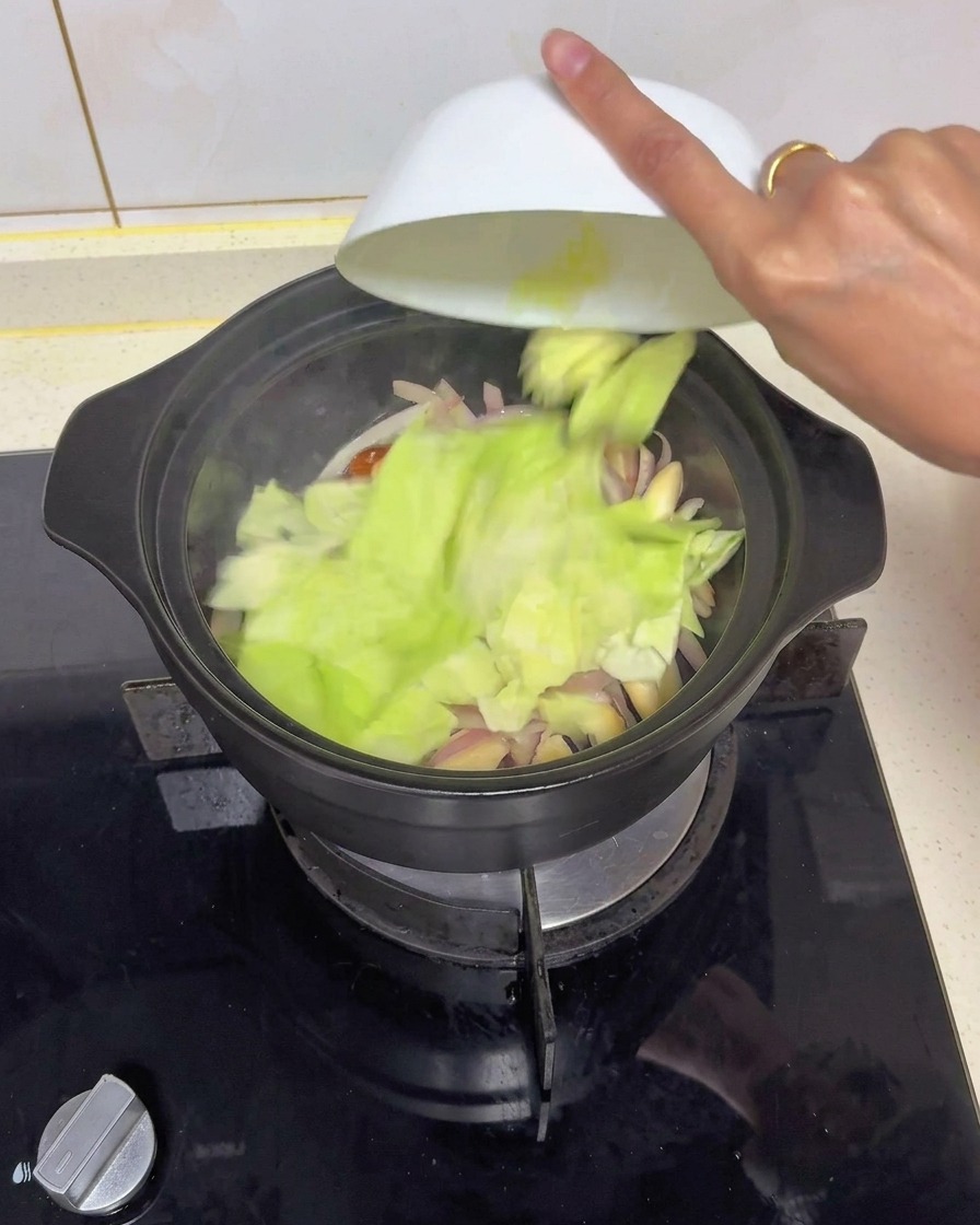Pezzi tagliati di cavolo cappuccio verde fresco svuotati da una ciotola bianca in una pentola nera con cipolle e funghi soffritti.