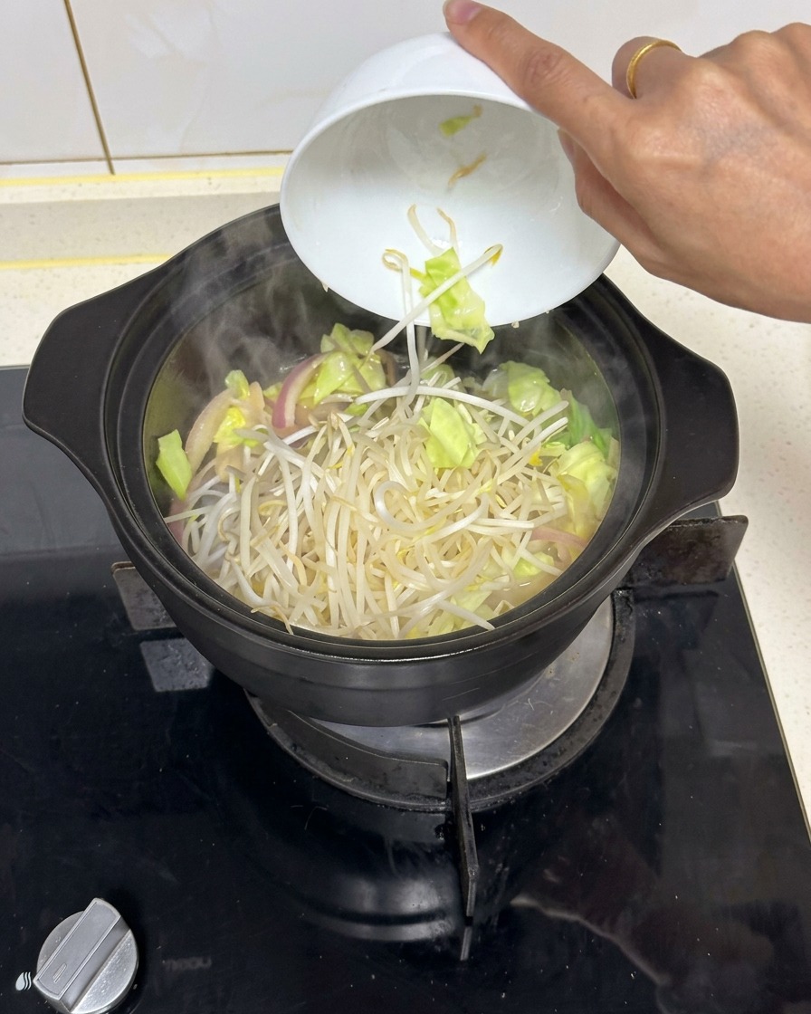 Una manciata di germogli di soia freschi fatti cadere da una ciotola di ceramica bianca in una pentola nera fumante con verdure saltate.