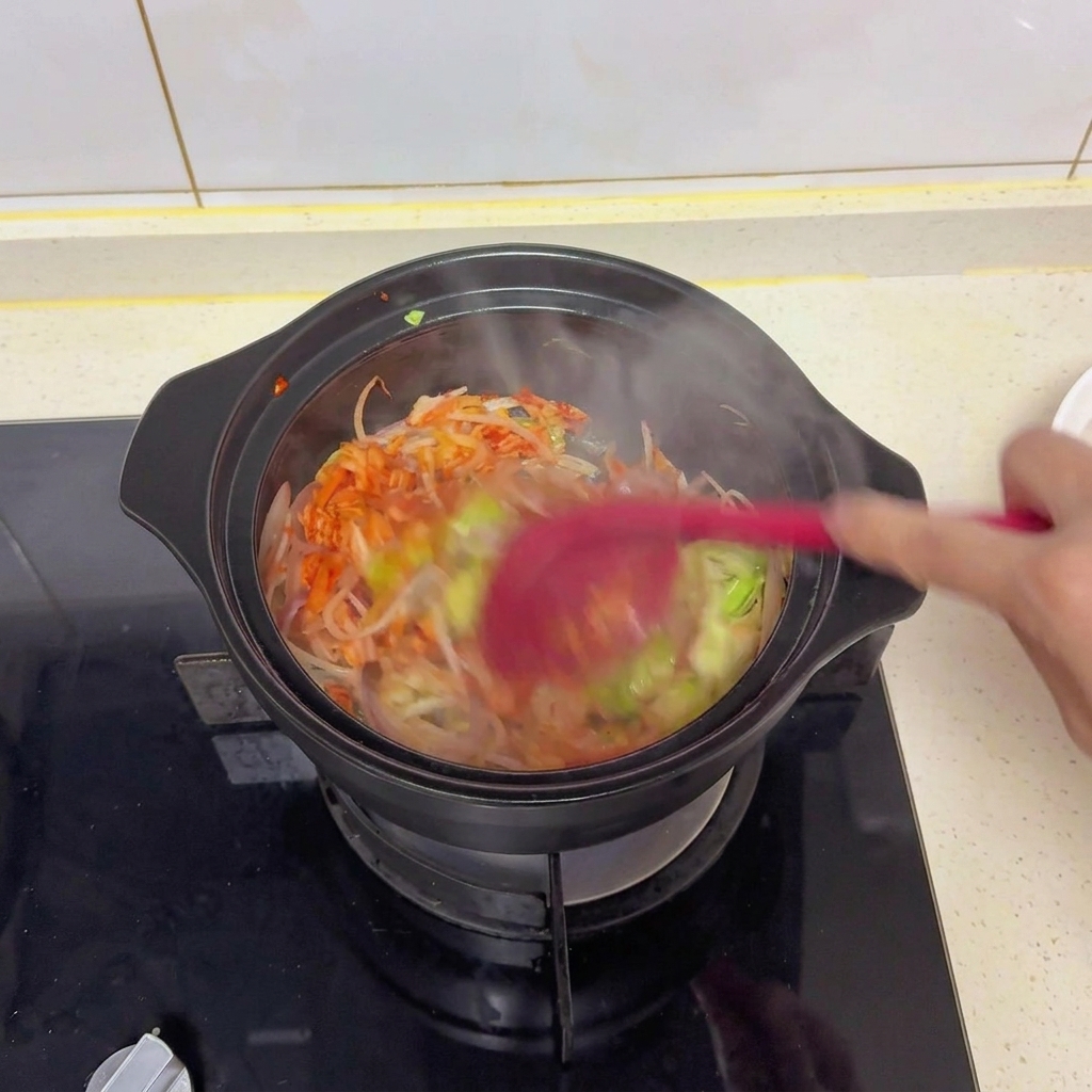 Verdure miste e kimchi saltati in una pentola nera con una spatola rossa per incorporare il sale, la salsa di soia e gli aromi.