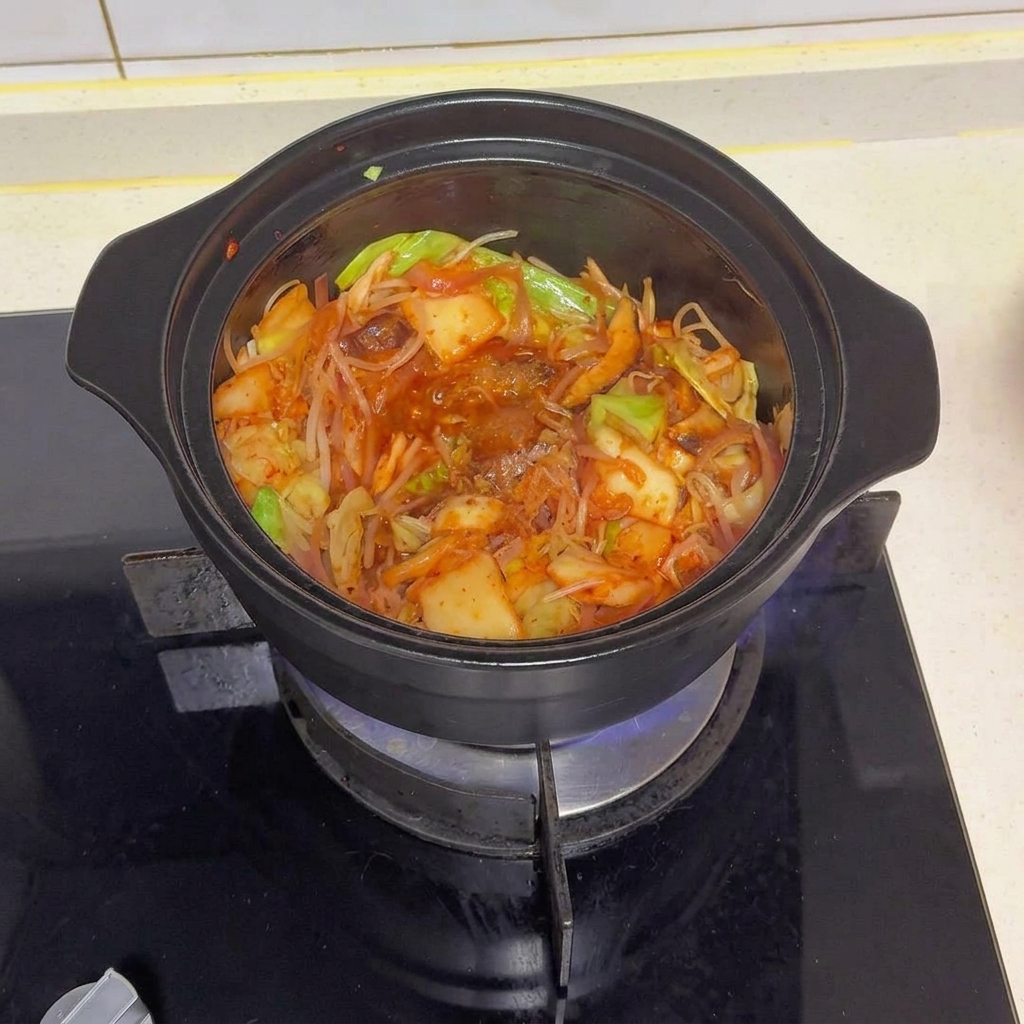 Una pentola nera piena di verdure saltate e kimchi, guarnita con vari condimenti e peperoncino rosso in polvere.