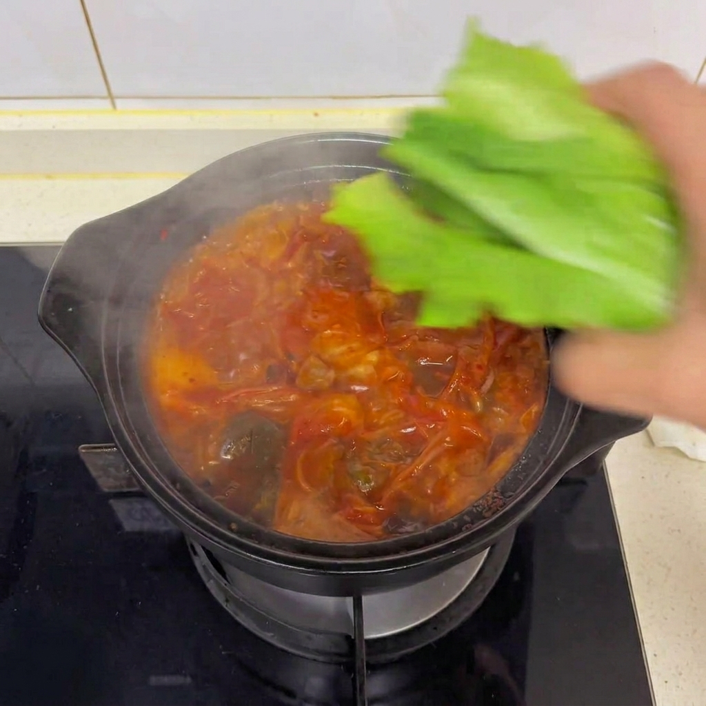 Una mano che adagia foglie fresche di lattuga romana verde in una pentola fumante di zuppa di kimchi e tofu.