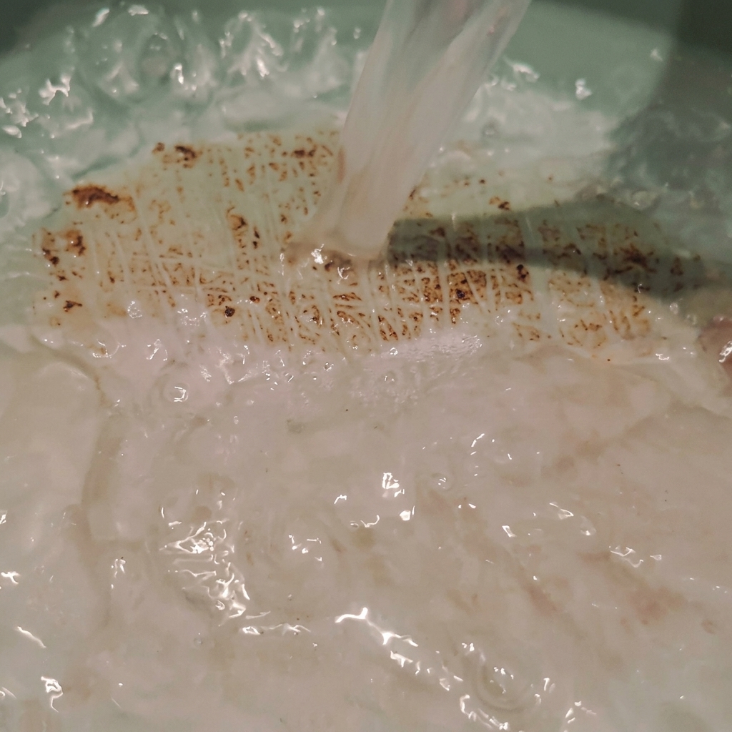 Acqua di riso opaca versata direttamente in una pentola, che crea lievi increspature e bolle nel liquido.