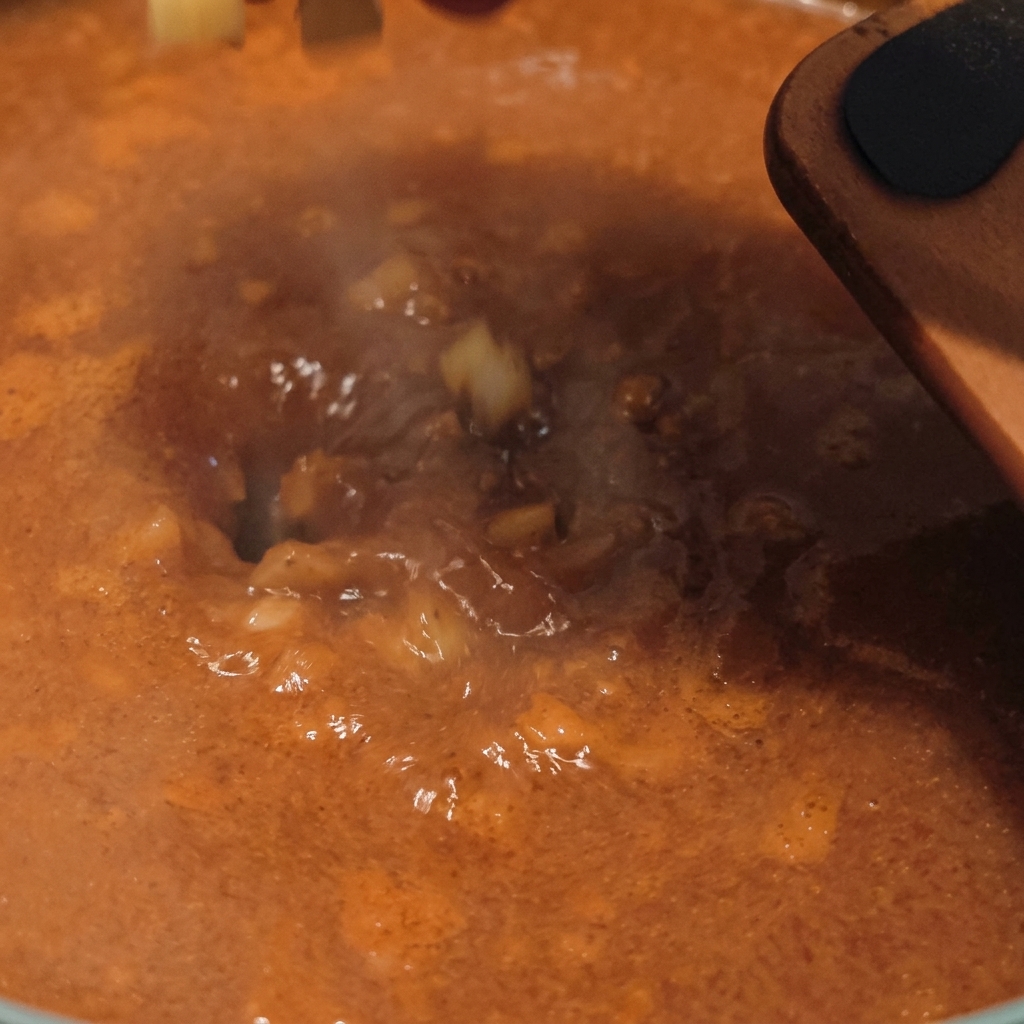 Patate crude a cubetti che vengono versate in una base di zuppa saporita e bollente di colore arancione, con il vapore che sale dalla pentola.