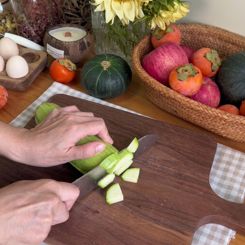 Un primo piano di mani che usano un coltello da chef per tagliare una zucchina verde a cubetti su un tagliere di legno.