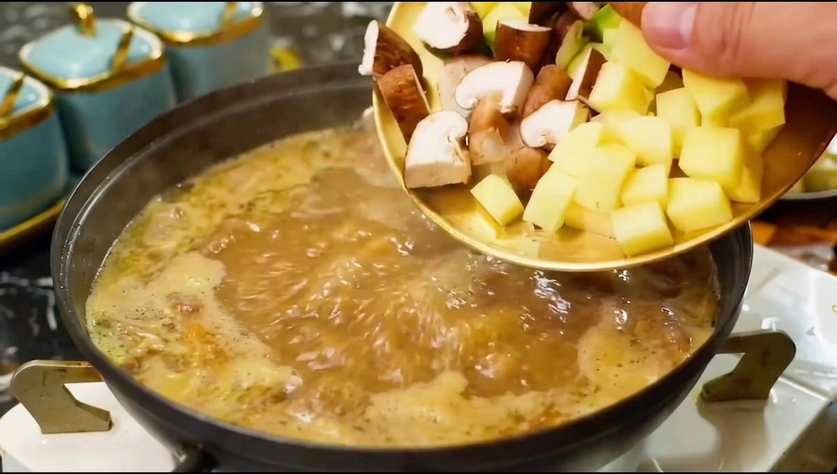 Funghi e verdure tagliati che vengono fatti scivolare da un piatto in una pentola di brodo bollente.