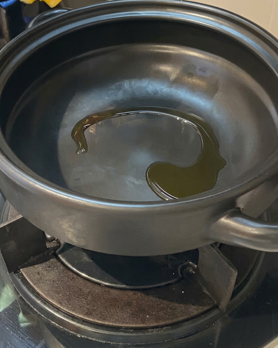 Olio di semi che brilla sul fondo di una pentola di terracotta nera calda su un fornello a gas.