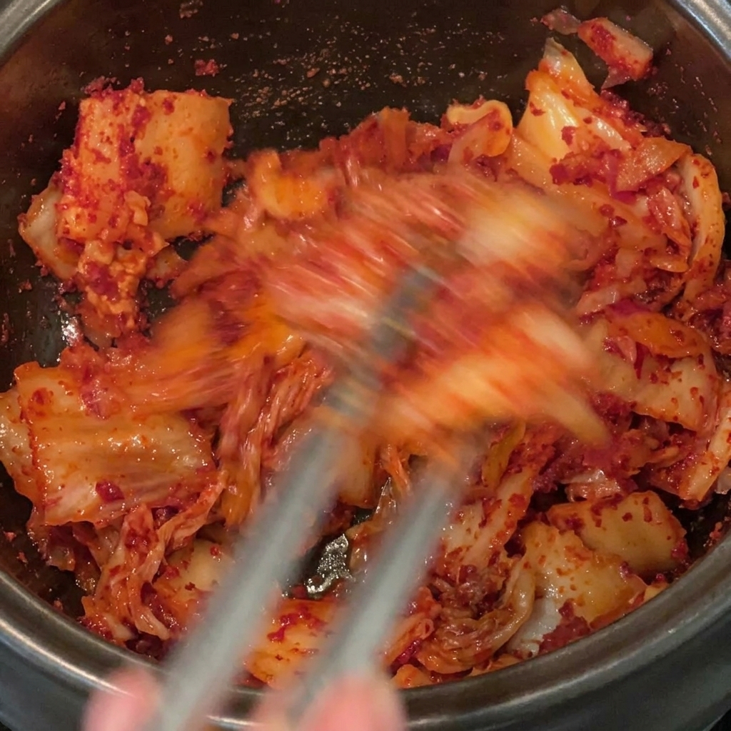 Mescolare accuratamente il peperoncino in polvere nel kimchi e nella pancetta allinterno di una pentola nera.
