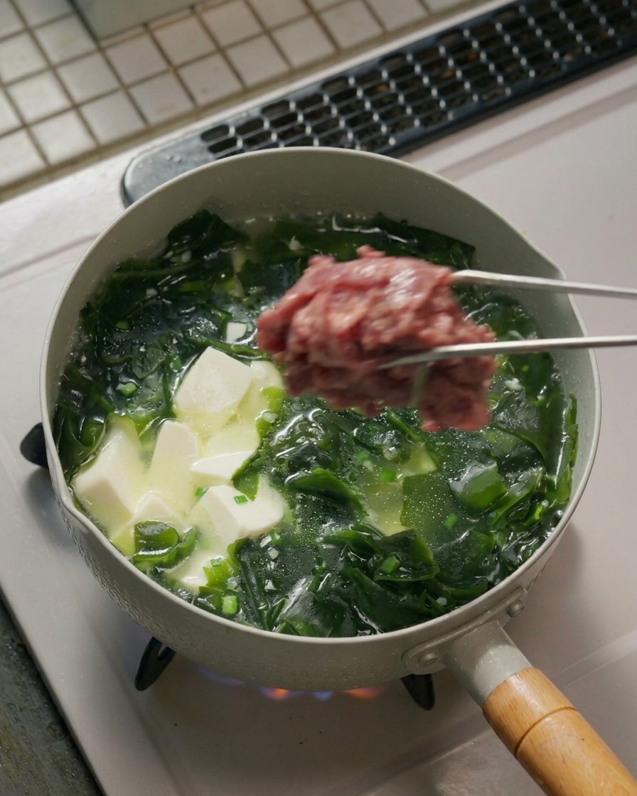 Manzo aggiunto alla zuppa con le pinze.