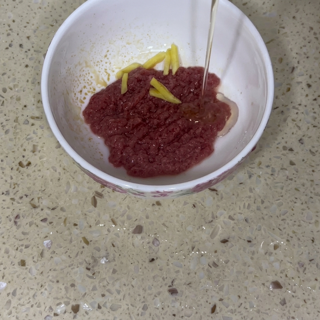Manzo macinato crudo in una ciotola di ceramica bianca con fette di zenzero, mentre viene versato un filo dolio per bambini.