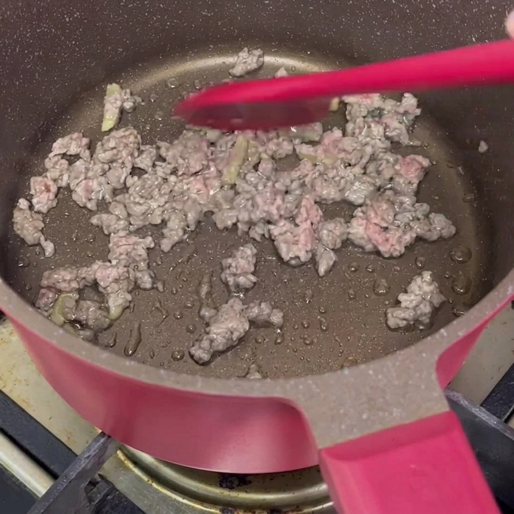 Manzo macinato marinato saltato con una spatola di silicone rossa in una pentola rosa finché non cambia colore.