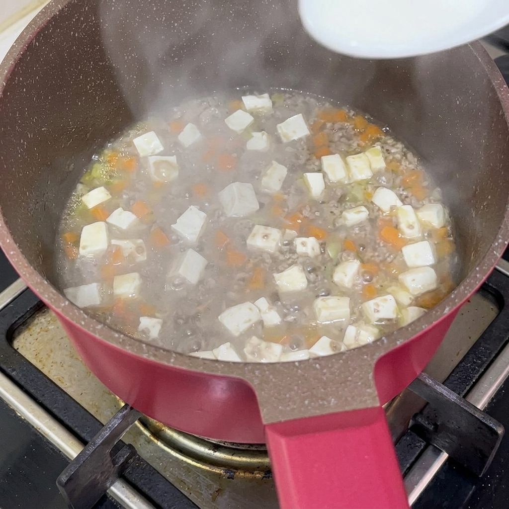 Un cucchiaio bianco versa una miscela di acqua e fecola in una pentola con manzo, tofu e carote per addensare il sughetto.