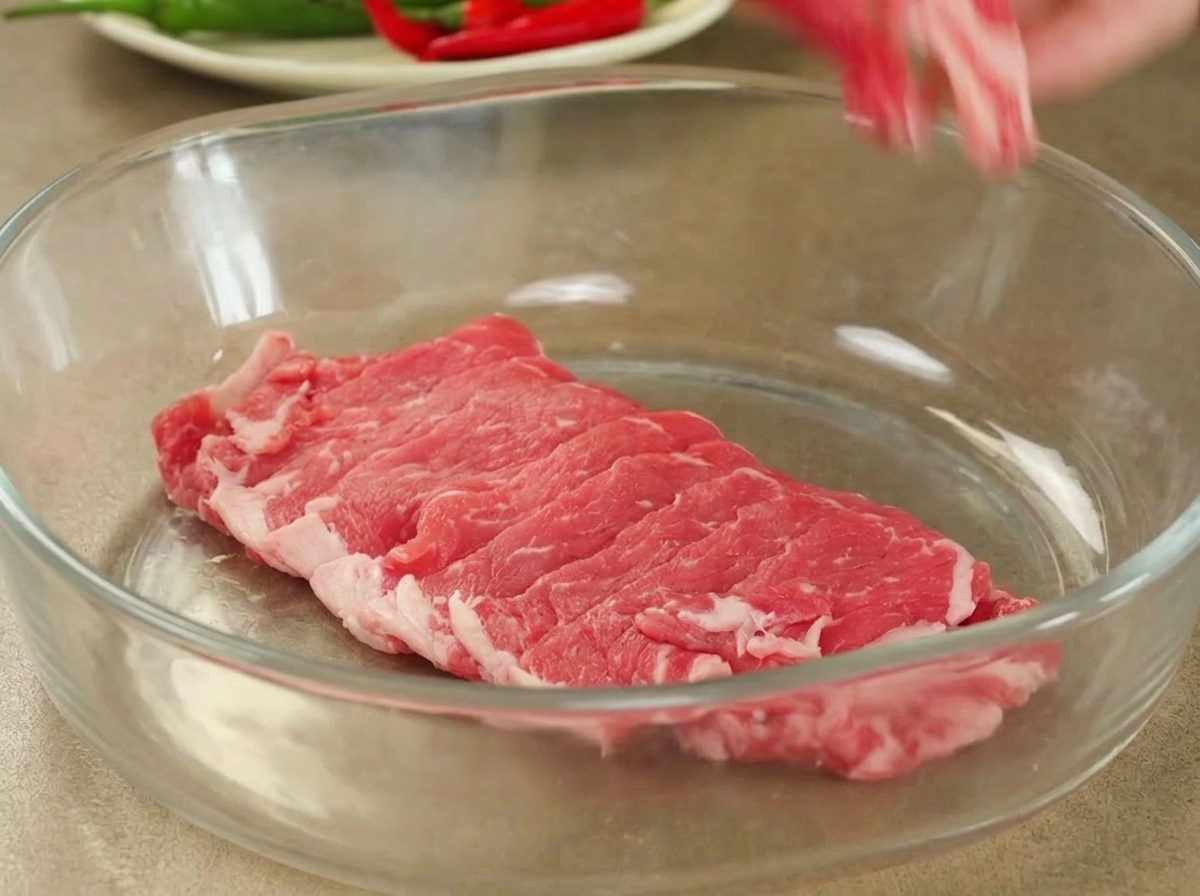 Manzo crudo affettato disposto ordinatamente in una ciotola di vetro pronto per la marinatura.