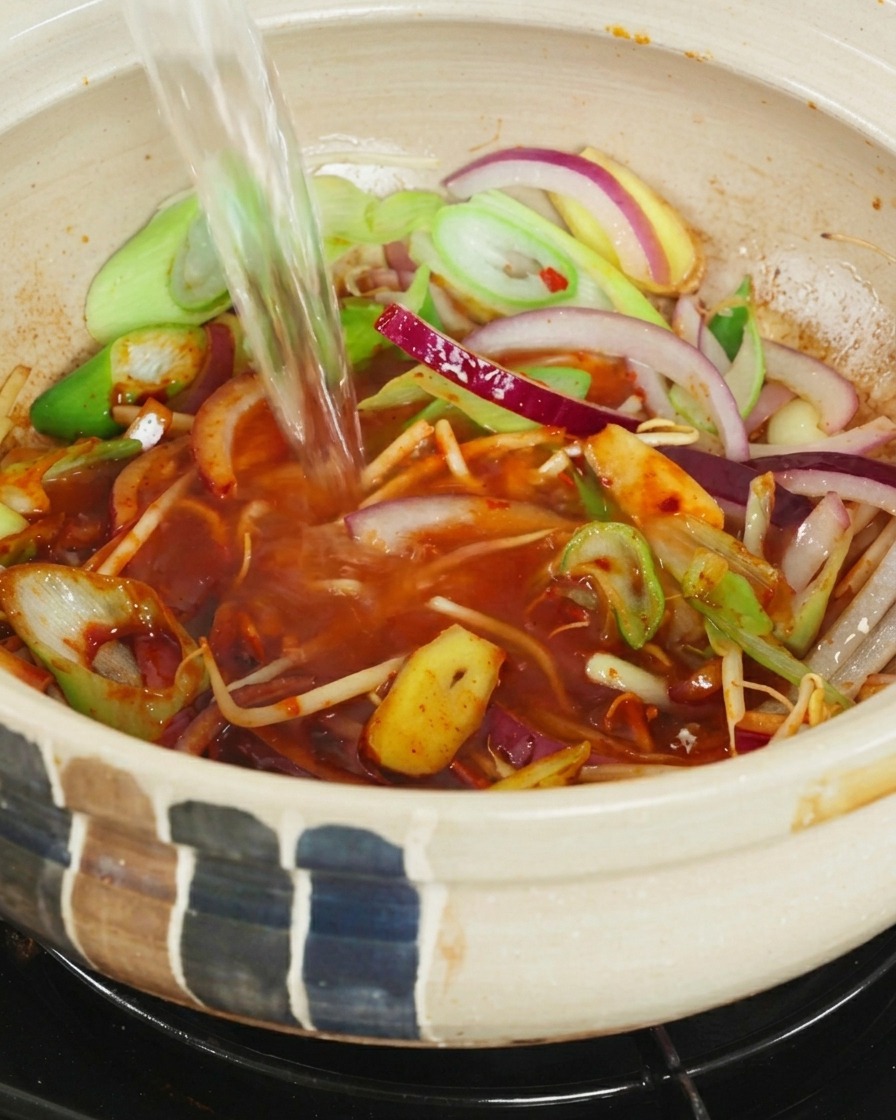 Acqua bollente versata nella pignatta con le verdure e la pasta al peperoncino.