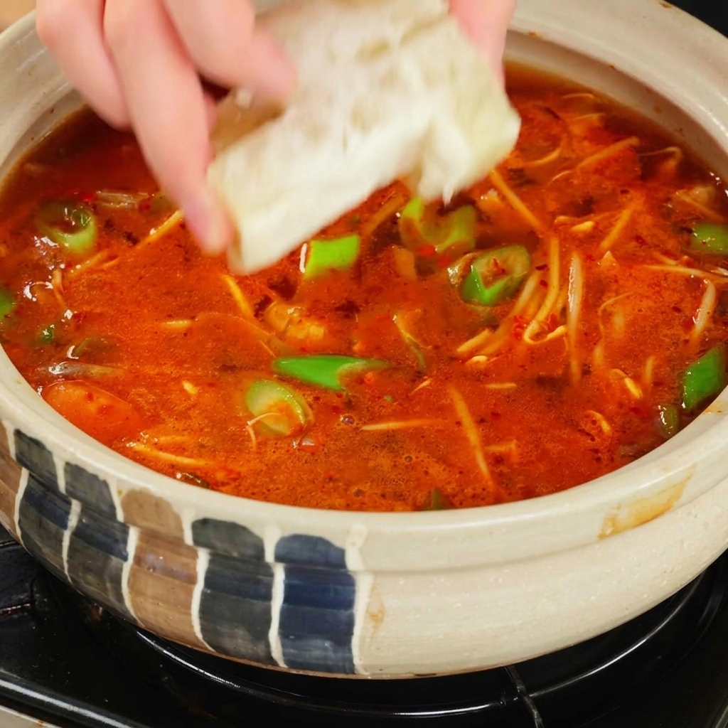 Una mano che lascia cadere un dado da brodo nella zuppa piccante in ebollizione.