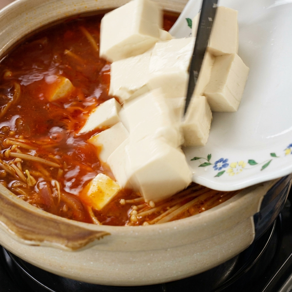 Cubetti di tofu inseriti nella zuppa bollente con funghi enoki.