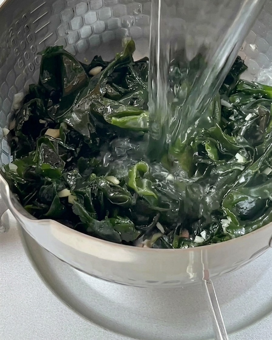 Acqua bollente versata da un bollitore di vetro sopra le alghe wakame in una pentola.