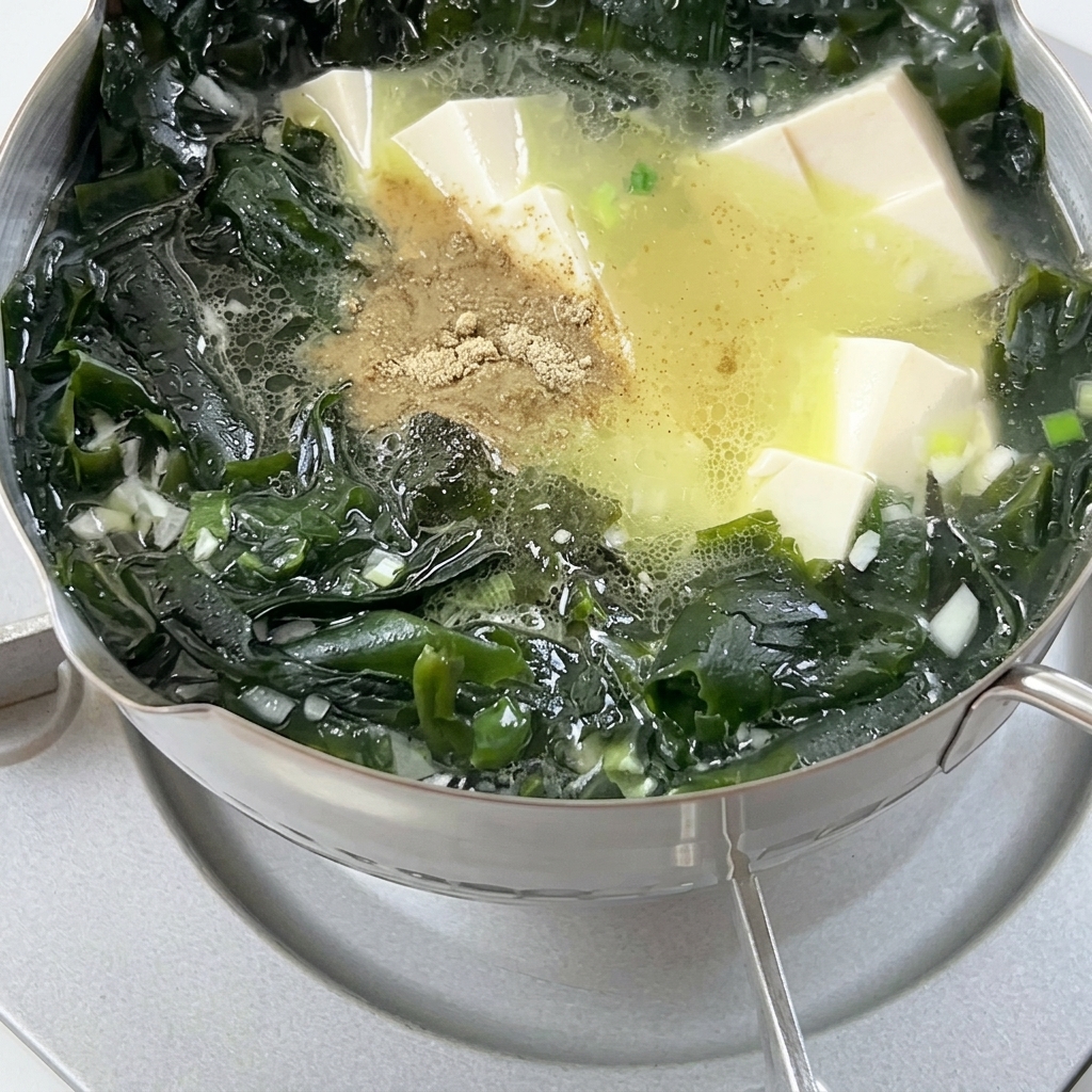 Pepe in polvere spolverato in una pentola di zuppa in ebollizione contenente alghe wakame e cubetti di tofu.