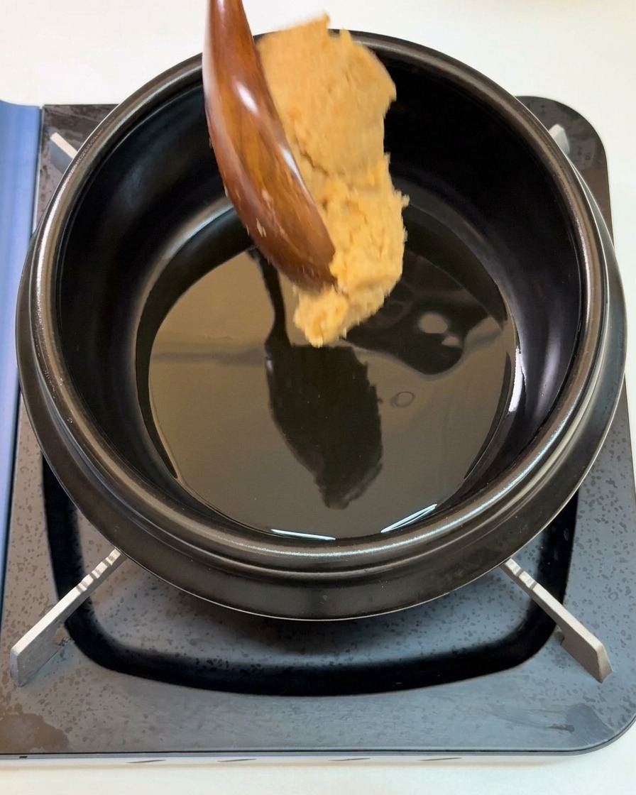 Un generoso cucchiaio di densa pasta di soia versato in un tegame nero con olio di sesamo caldo.