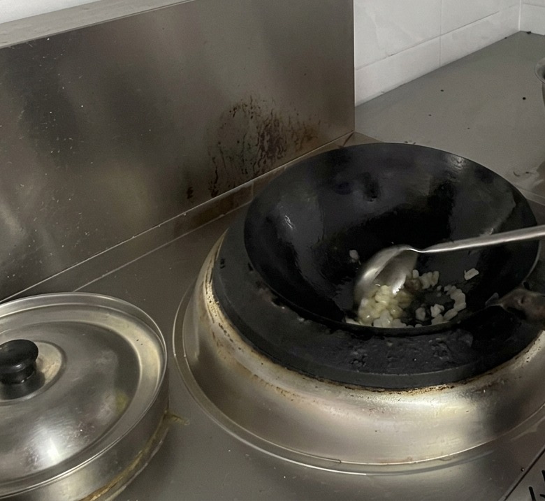 Un cuoco usa un grande mestolo di metallo per mescolare i pezzi di zucchero candito che si sciolgono in un wok.