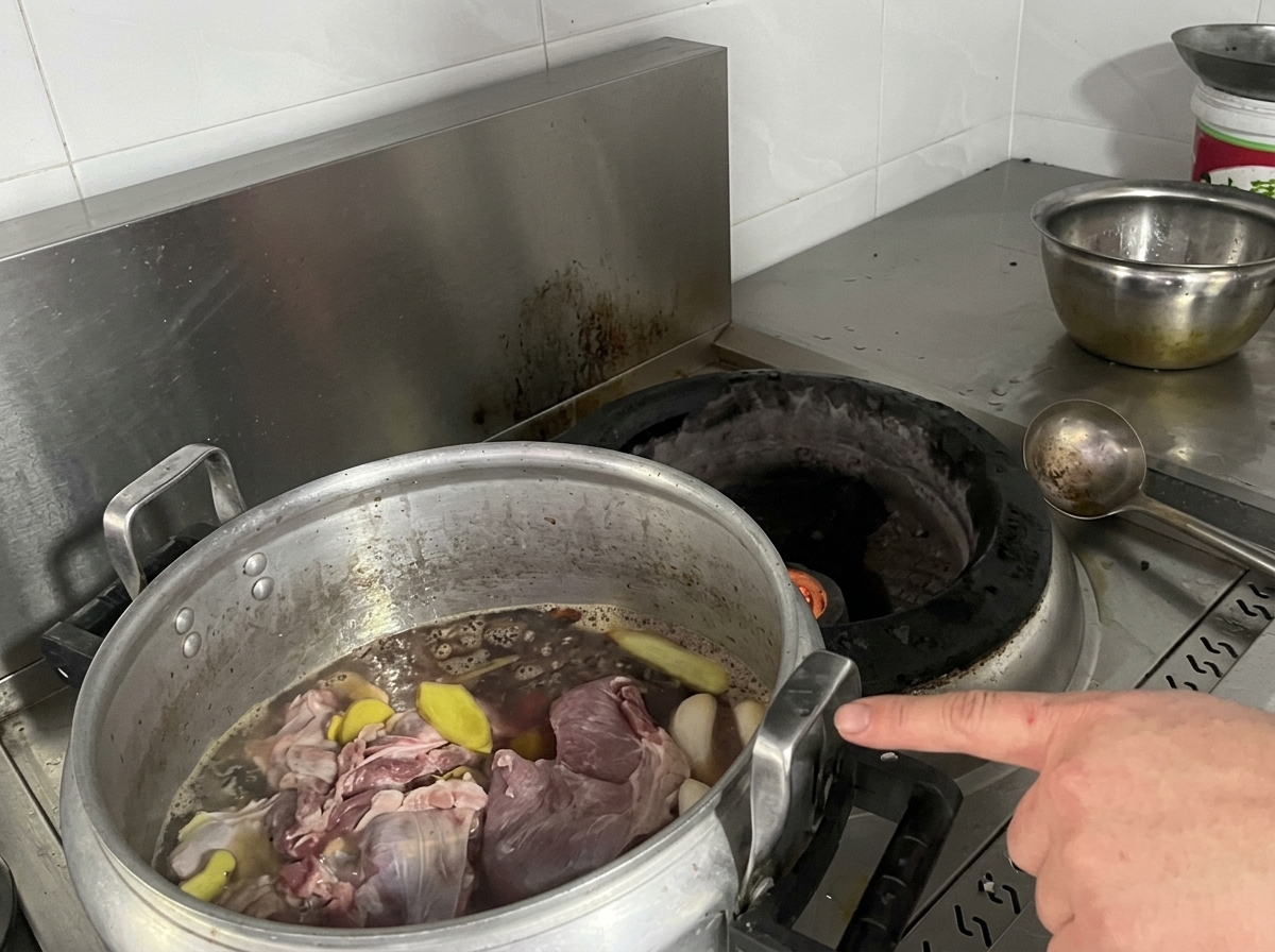 Una grande pentola di alluminio piena di carne cruda, fette di zenzero e brodo scuro appoggiata su un fornello.