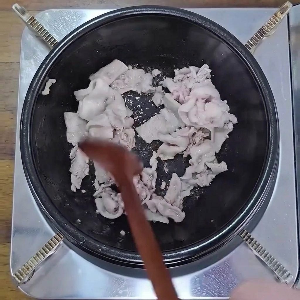 Pancetta a fette sottili che soffrigge in una pentola nera con un cucchiaio di legno finché non è leggermente dorata.