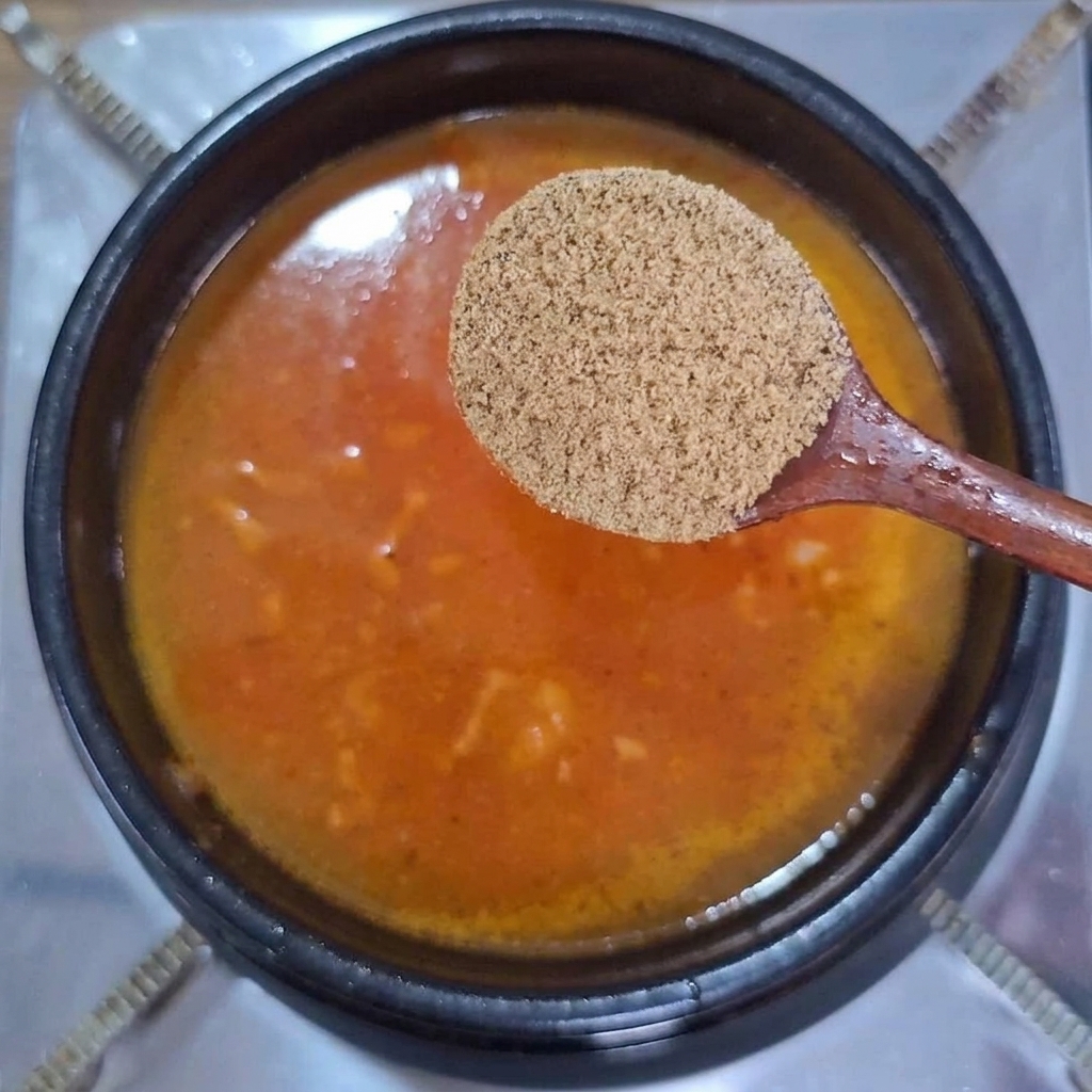 Cucchiaio di legno che sostiene polvere di brodo di manzo sopra una pentola di brodo bollente arancione.