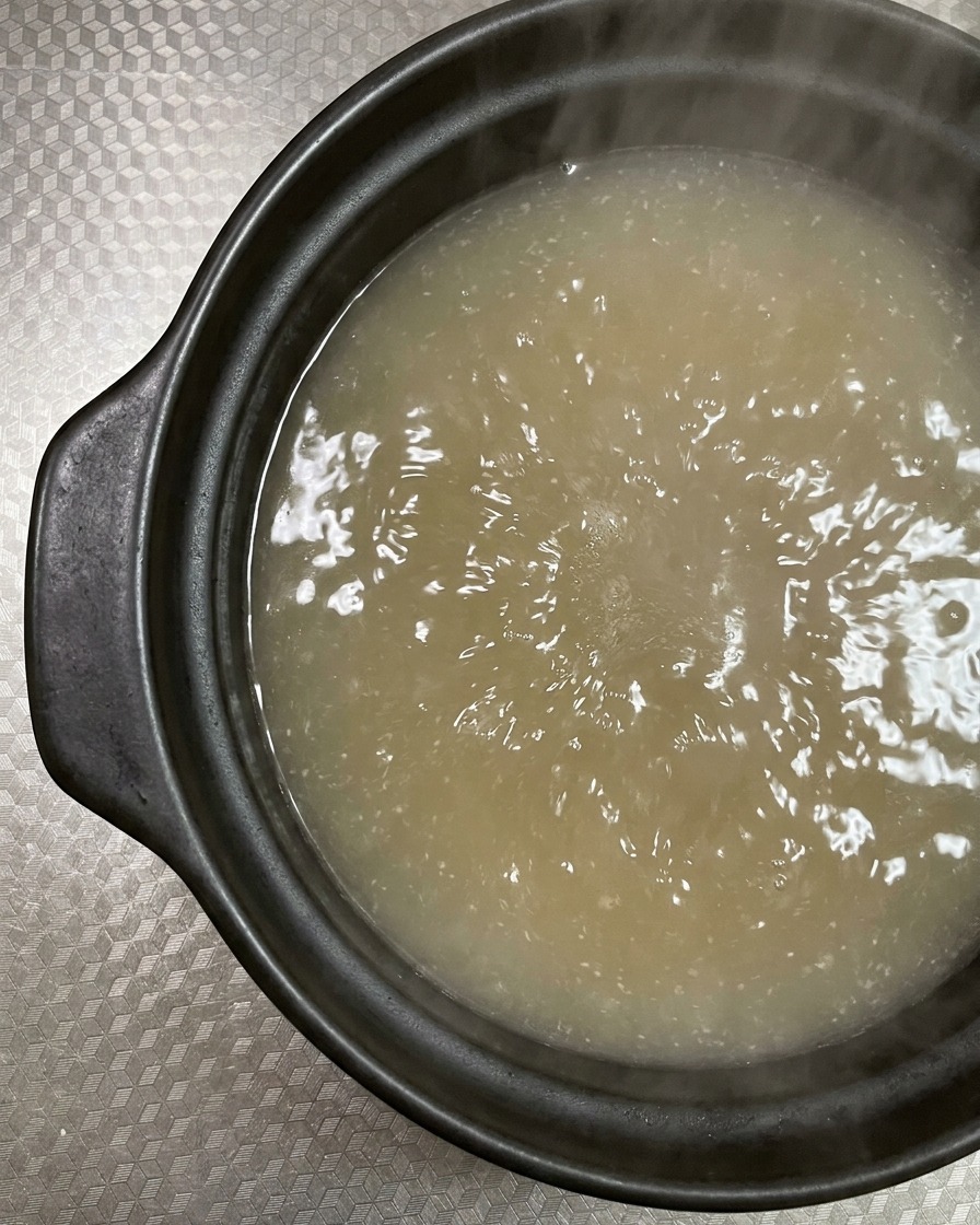 Fette di pancetta cruda venata poste in una pentola di terracotta con brodo in ebollizione.