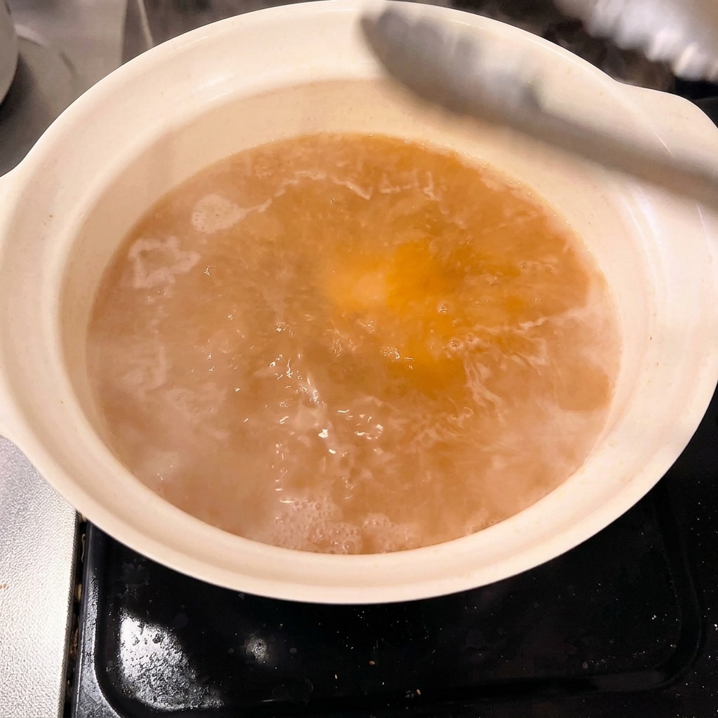 Grossi pezzi di pancia di maiale sbollentata vengono riposti con cura in una pentola piena di brodo di miso.