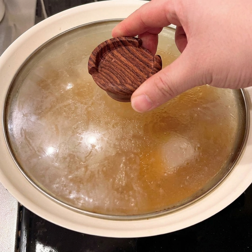 Un piccolo coperchio di legno viene posizionato direttamente sui bocconcini di maiale che sobbollono nel brodo saporito.