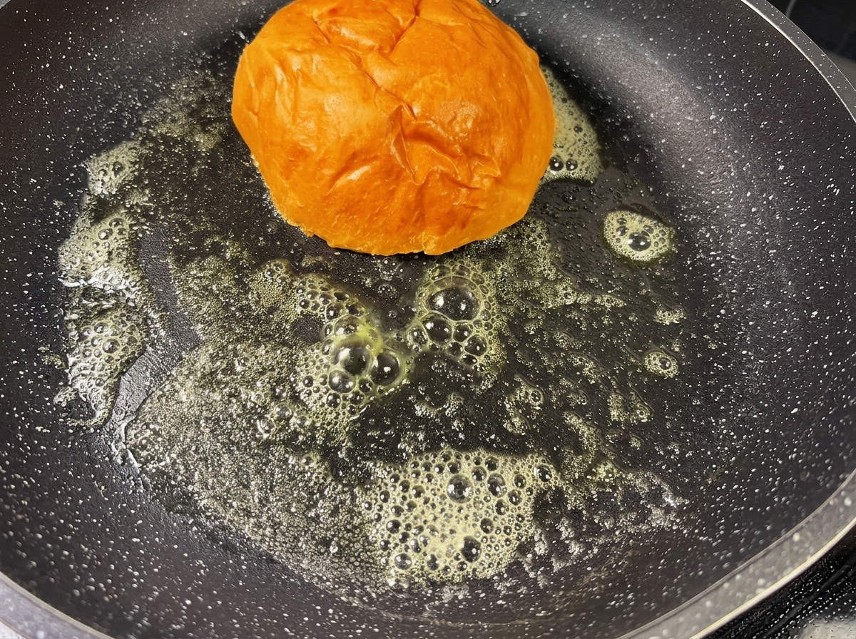 Un panino per hamburger viene tostato in una padella calda con burro fuso, diventando dorato.