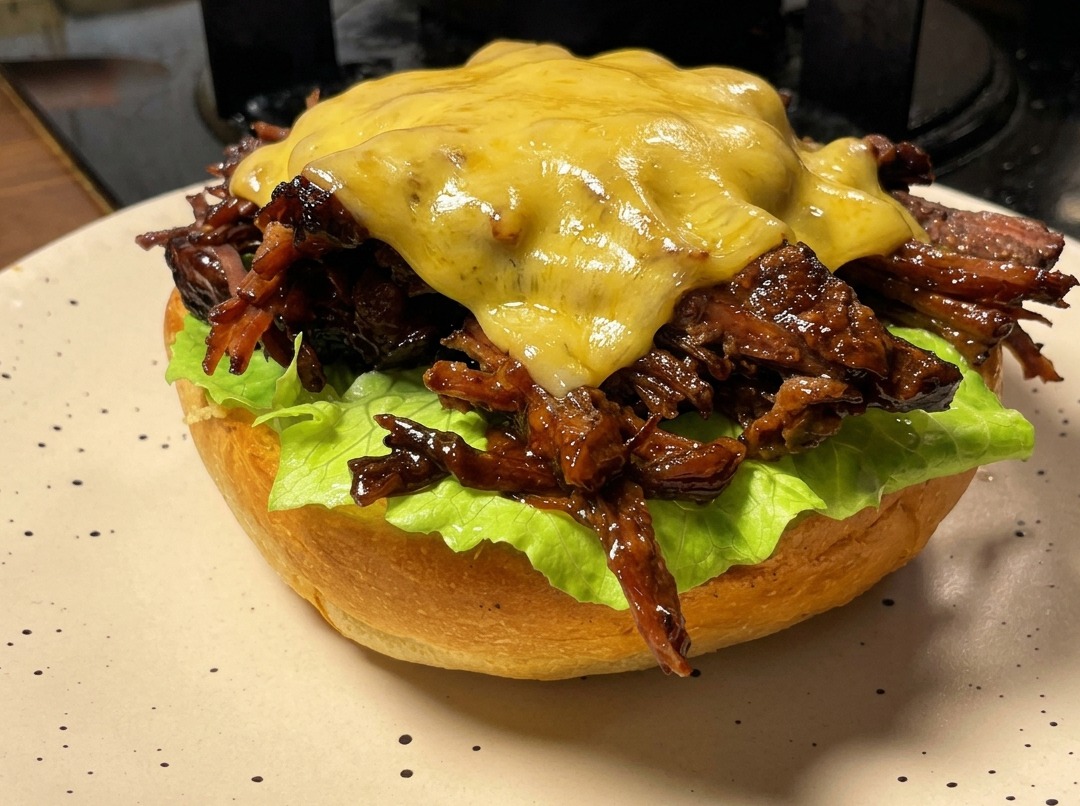 Un hamburger di pulled beef con una fetta di formaggio che viene fusa con un cannello da cucina.