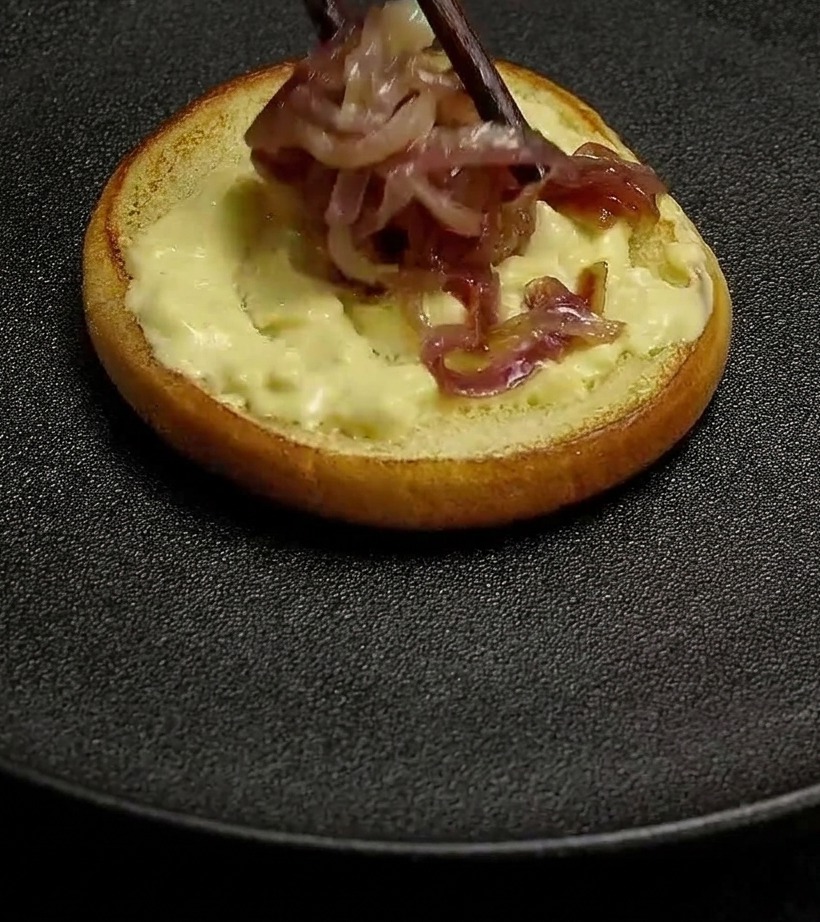 Anelli di cipolla rossa cotta posizionati con le bacchette sulla base di un panino spalmata con salsa cremosa.