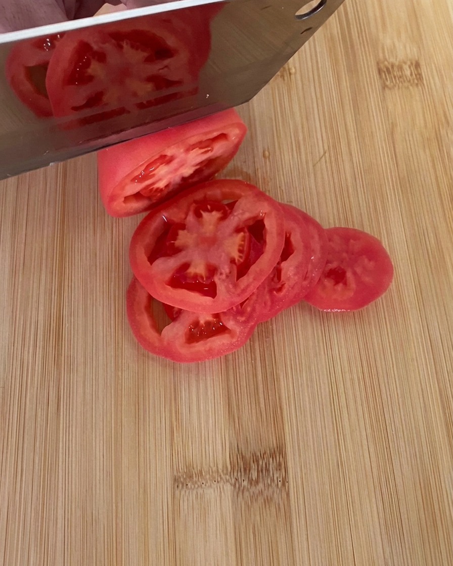 Un coltello che affetta un pomodoro rosso maturo in fette spesse su un tagliere di legno.