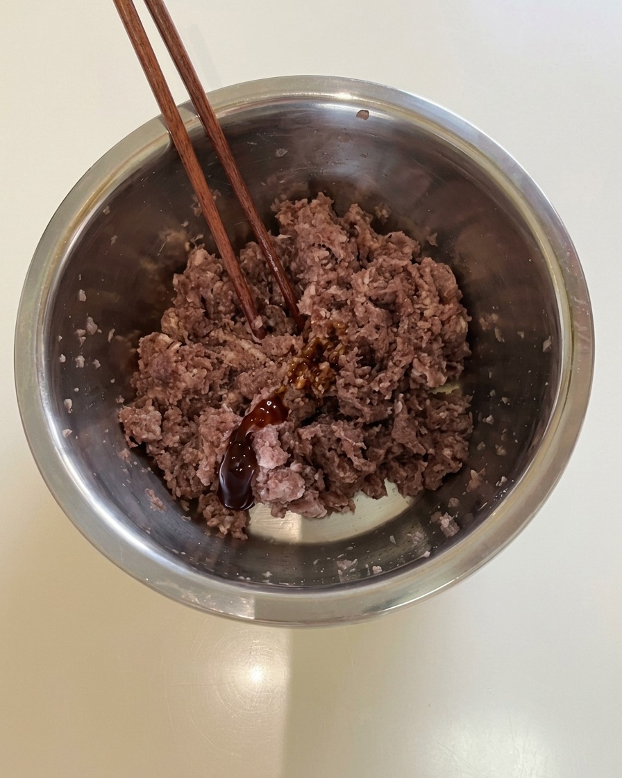 Bacchette appoggiate in una ciotola di metallo piena di carne di manzo speziata e salsa scura.