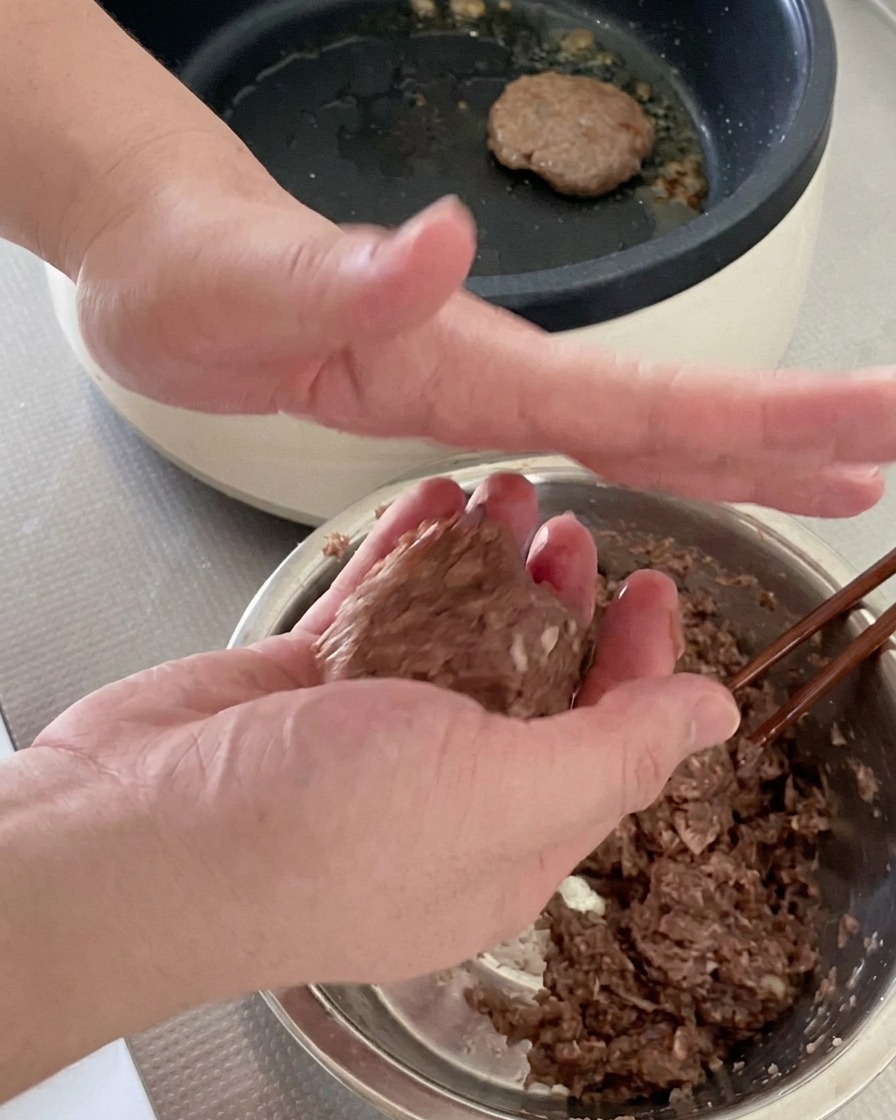 Due mani che lanciano e modellano una palla di carne di manzo cruda in un disco da hamburger.