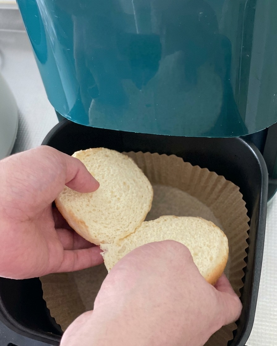 Due metà di un panino per hamburger messe nel cestello di una friggitrice ad aria foderato con carta forno.