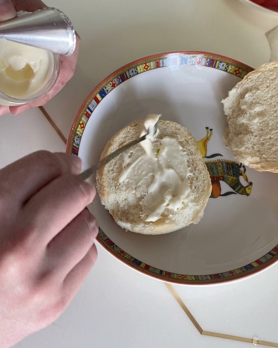 Un primo piano di un cucchiaio che spalma il condimento cremoso per insalata sul pane dellhamburger.