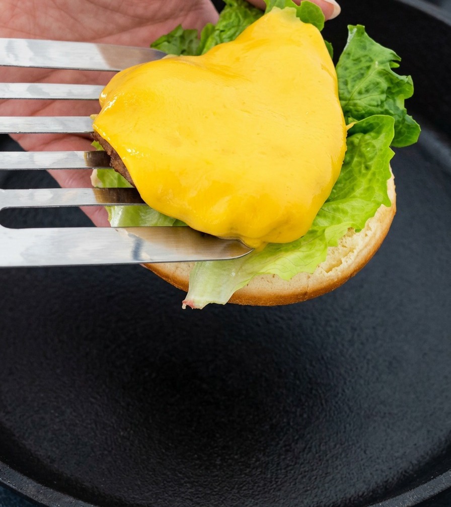 Una spatola di metallo che solleva lhamburger al formaggio per posizionarlo sul pane.