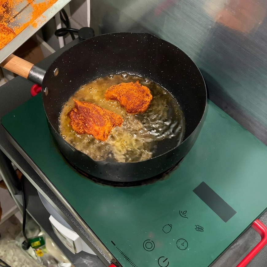 Bocconcini di maiale speziati che sfrigolano in olio caldo allinterno di una padella nera su un fornello a induzione.