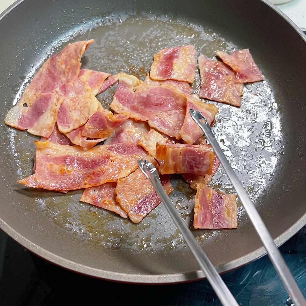 Uova sbattute in cottura in padella con pezzi di bacon.