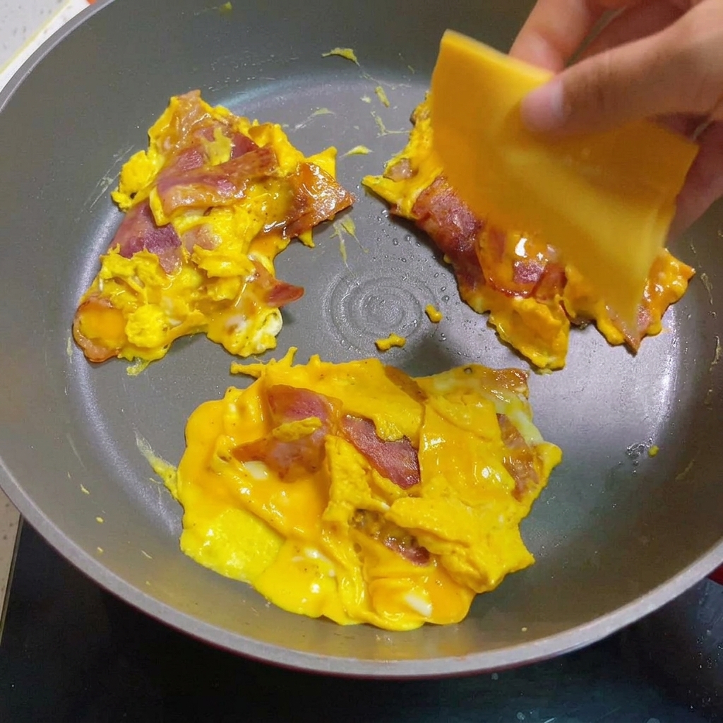 Uova strapazzate e bacon sormontati da fette di formaggio in fase di fusione.