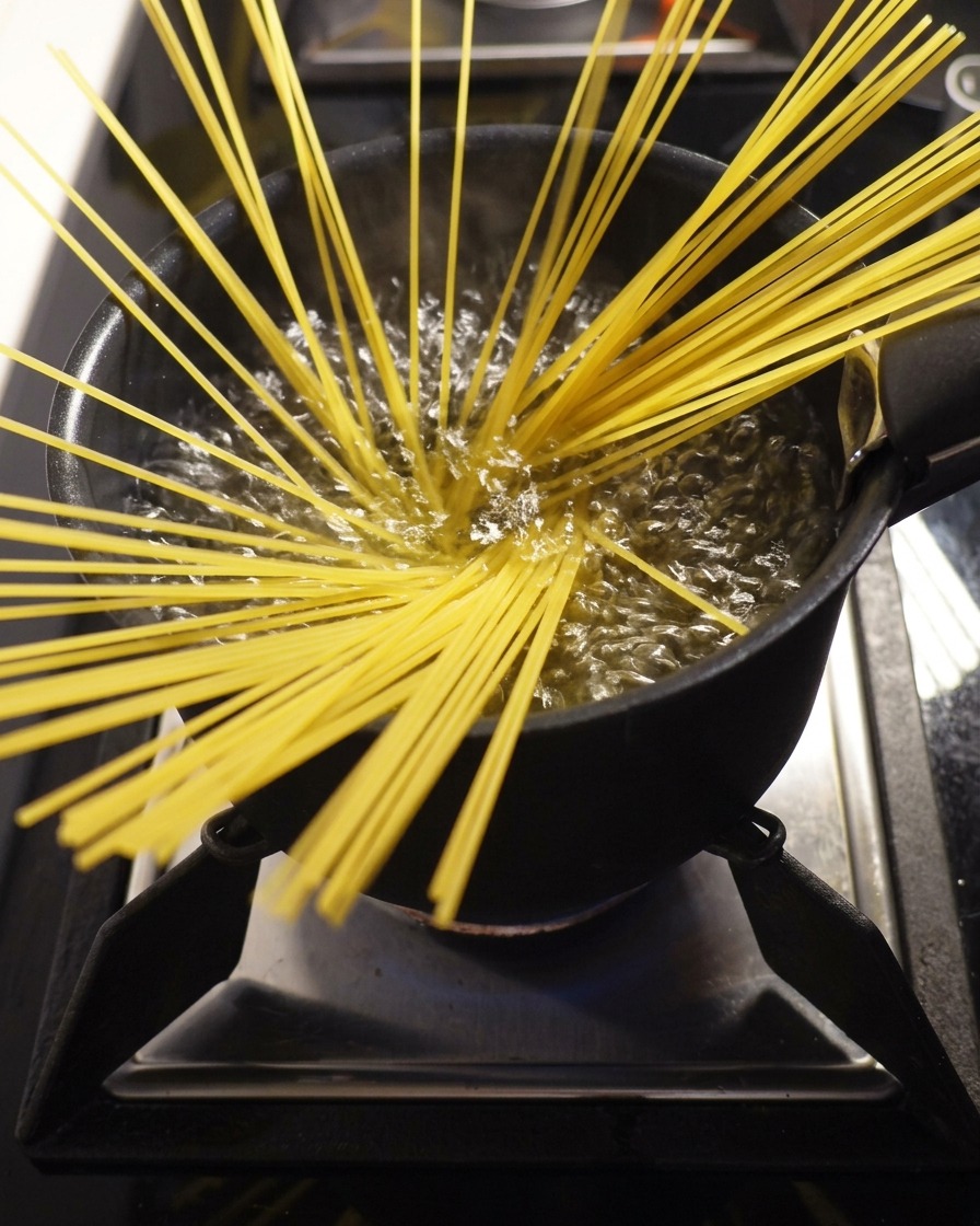 Spaghetti secchi immersi in una grande pentola di acqua bollente.