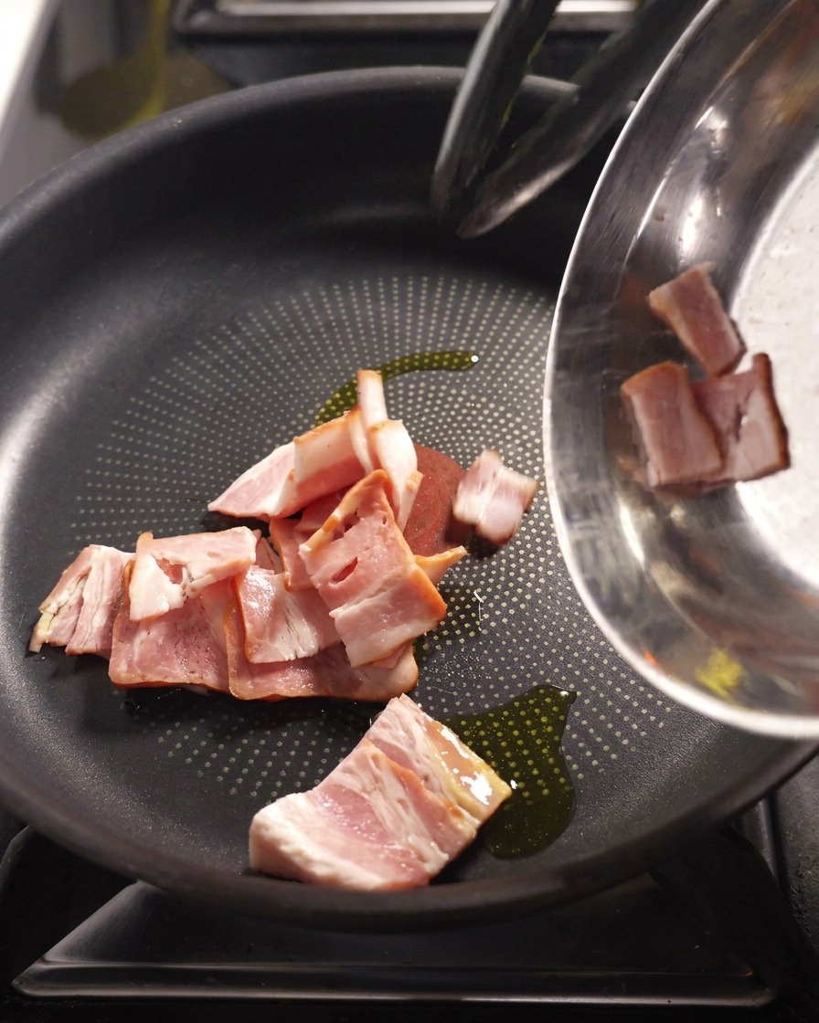 Strisce di pancetta che sfrigolano in padella fino a diventare dorate e croccanti.