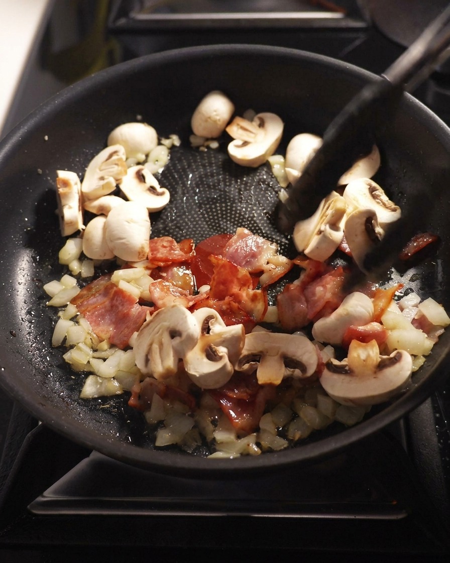 Funghi champignon affettati saltati in padella con pancetta, cipolla e aglio.